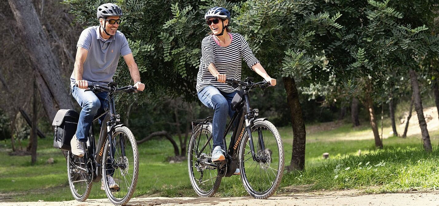 Eine Frau und ein Mann fahren auf Elektrofahrrädern durch den Wald. 